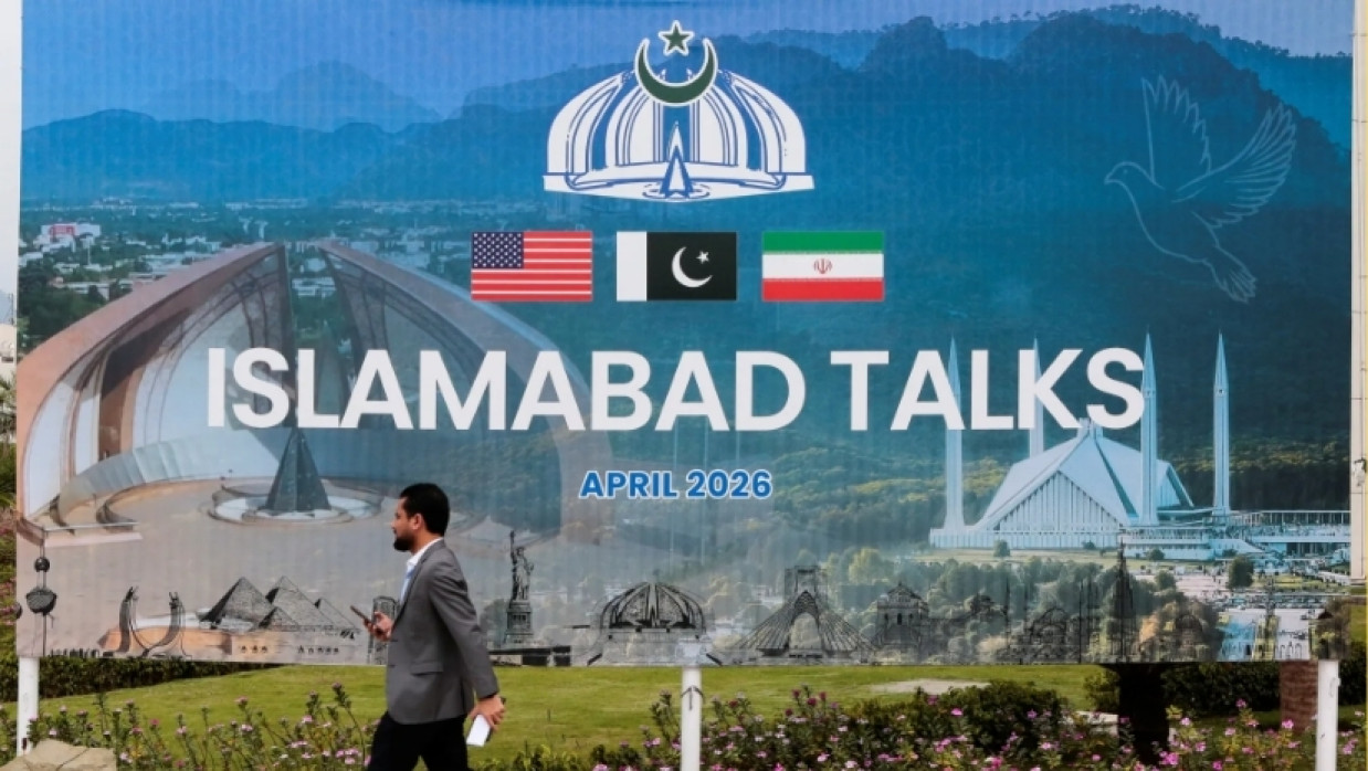 A man walks past a billboard announcing US and Iran negotiations outside a media centre in Islamabad