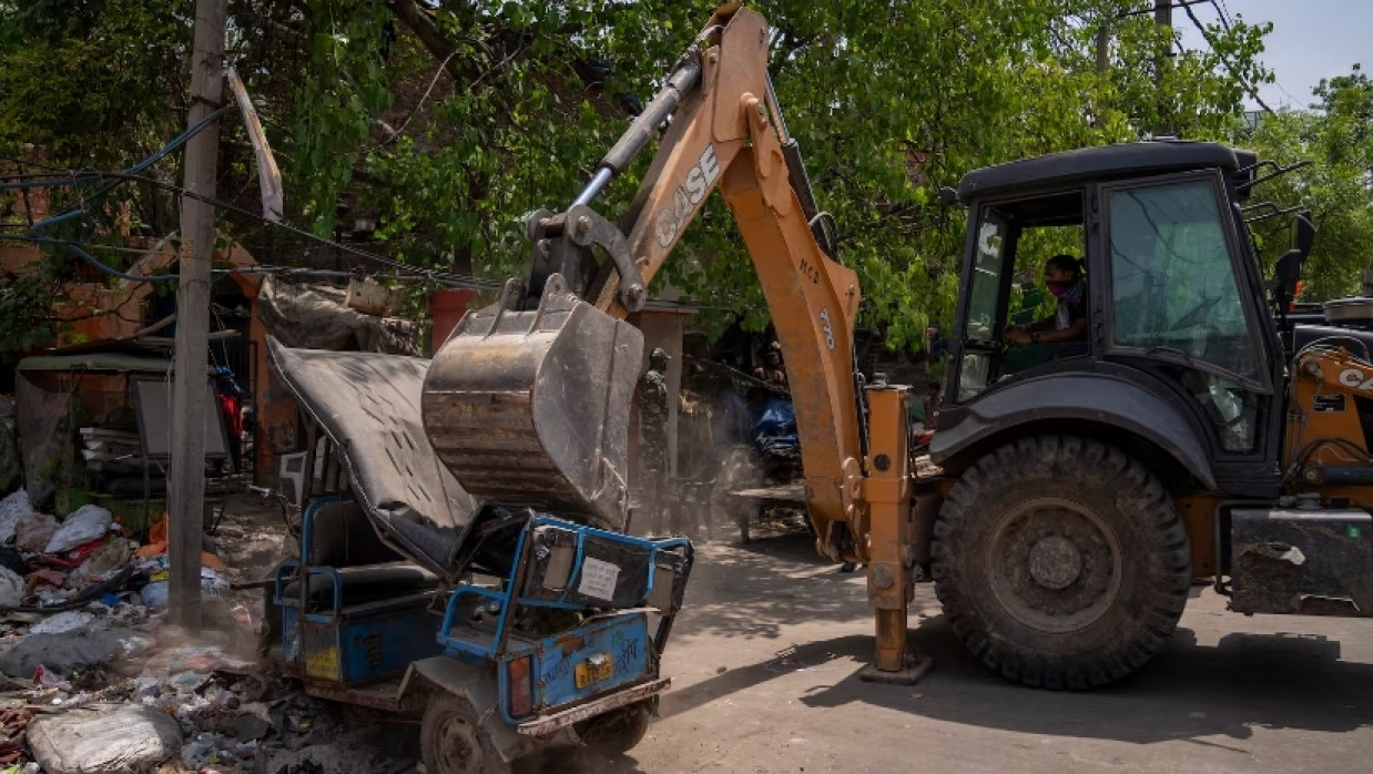 A bulldozer slams an auto rickshaw during the demolition of Muslim-owned shops in the area