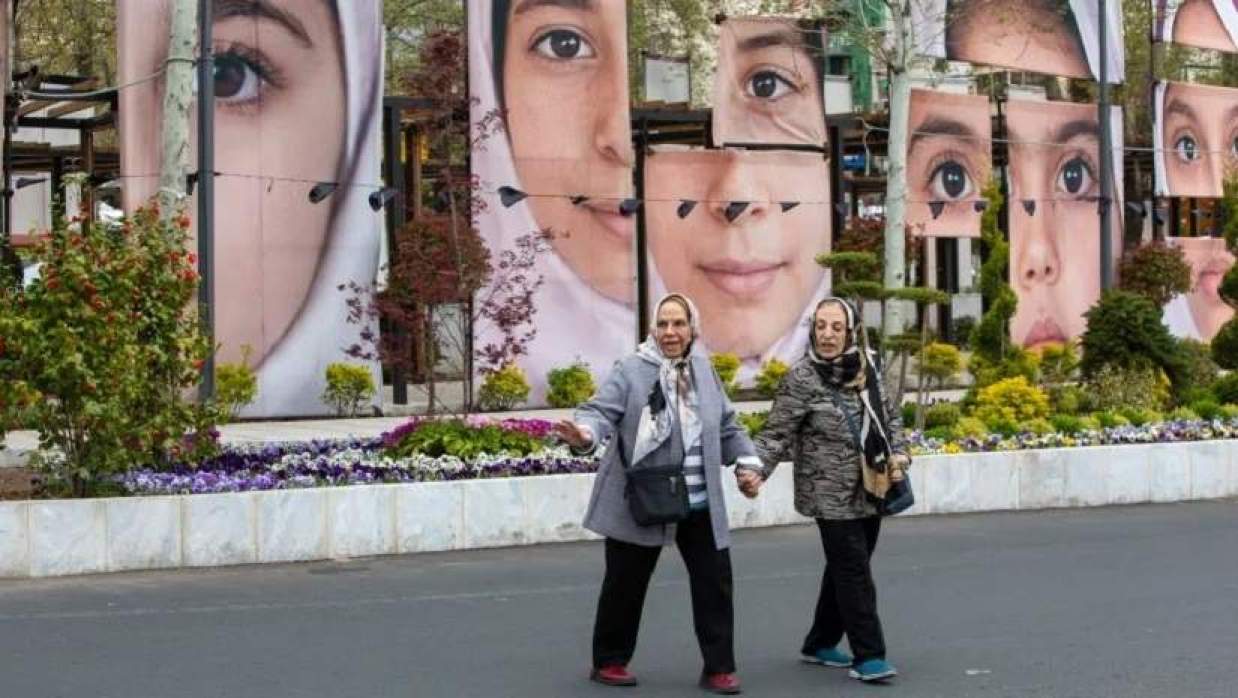 তেহরানে ফেব্রুয়ারিতে মার্কিন-ইসরায়েলি হামলায় নিহত মিনাবের স্কুলছাত্রীদের প্রতিকৃতি সংবলিত একটি স্থাপনার পাশ দিয়ে হেঁটে যাচ্ছেন দুই নারী