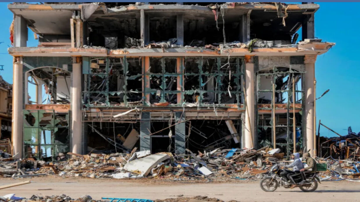 গাজা শহরের বিধ্বস্ত একটি ভবনের সামনে দিয়ে মটরসাইকেল চালিয়ে যাচ্ছেন দু’জন